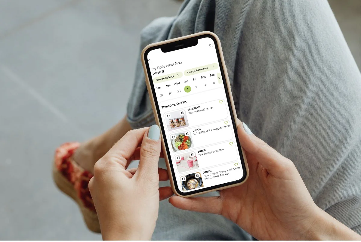 Hands holding a phone showing the TPNL app’s daily meal plan with breakfast, lunch, snack, and dinner